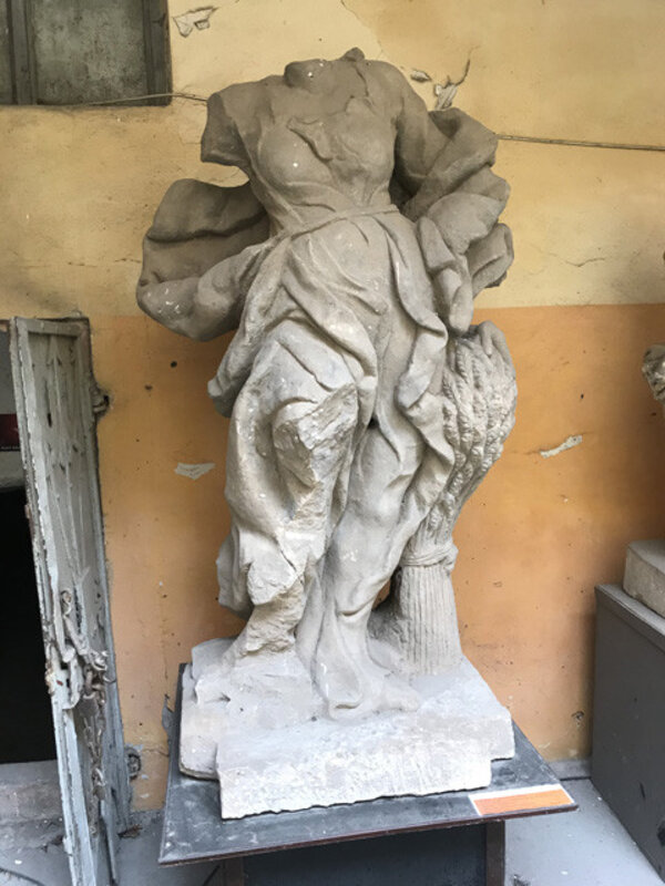 Fragment skulptury znázorňující alegorii Léta ukazuje ženskou postavu, která se levicí dotýká klasů obilného snopu. 